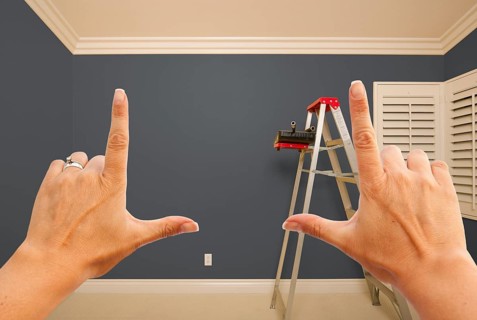 Hands framing grey painted room wall interior with ladder