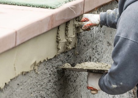 Tile worker applying cement with trowel at pool construction site