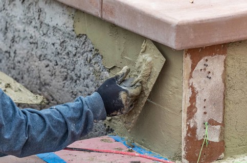 Tile worker applying cement with trowel at pool construction site