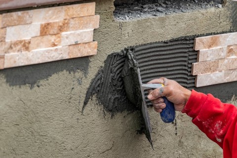 Worker installing wall tile cement with trowel and tile at construction site