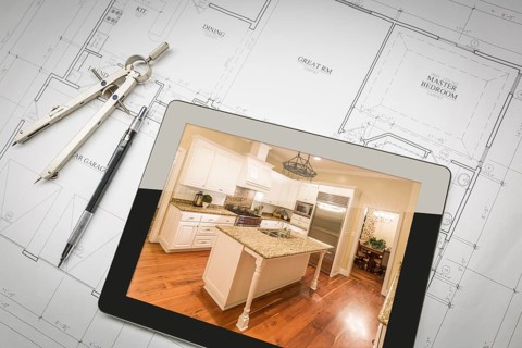 Computer tablet showing finished kitchen sitting on house plans with pencil and compass