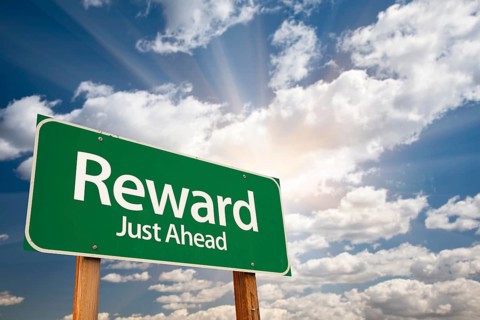 Reward green road sign against clouds and sunburst
