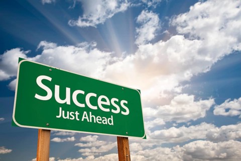 Success green road sign against clouds and sunburst