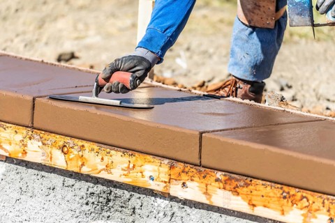 Construction worker using trowel on wet cement forming coping around new pool