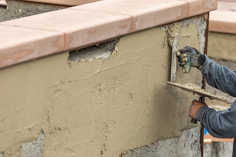 Tile worker applying cement with trowel at pool construction site