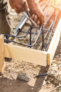 Worker securing steel rebar framing with wire plier cutter tool at construction site