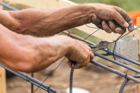 Worker securing steel rebar framing with wire plier cutter tool at construction site