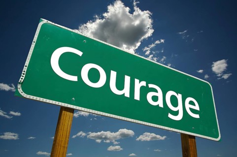 Courage green road sign over dramatic clouds and sky