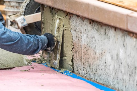 Tile worker applying cement with trowel at pool construction site