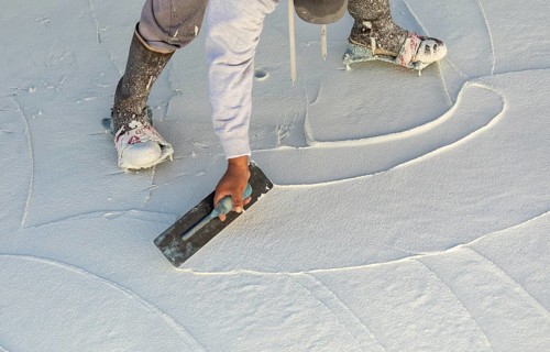 Worker wearing spiked shoes smoothing wet pool plaster with trowel