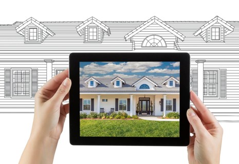 Female hands holding computer tablet with house photo on screen & drawing behind
