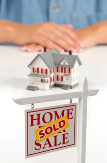 Womans folded hands behind model house and sold home for sale real estate sign in front on white surface