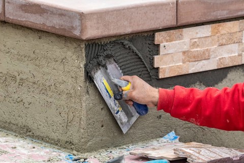 Worker installing wall tile cement with trowel and tile at construction site