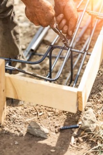 Worker securing steel rebar framing with wire plier cutter tool at construction site