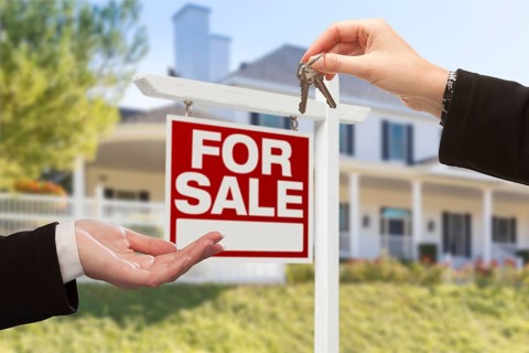 Real estate agent handing over the house keys in front of a beautiful new home and for sale real estate sign