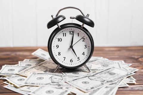 Alarm clock on spread currency notes over wooden textured background