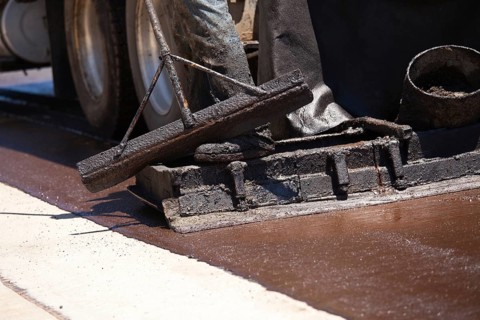 Road worker resurfacing street with hot tar