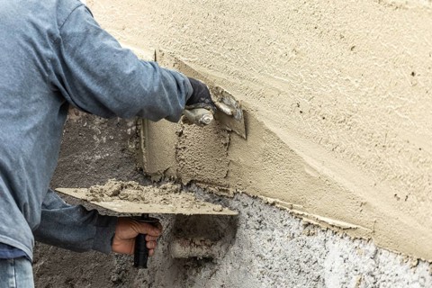 Tile worker applying cement with trowel at pool construction site