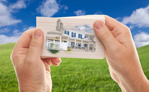 Male hands holding stack of paper with house drawing over empty grass field and sky