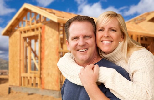 Happy excited couple in front of their new home construction framing site