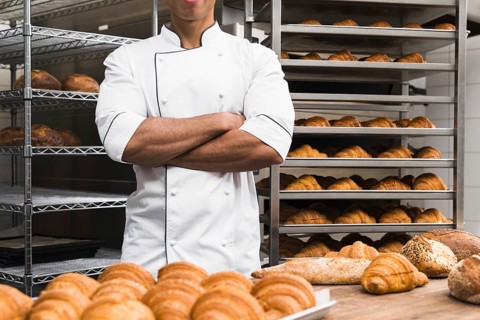 midsection male baker with his arms crossed standing bakery