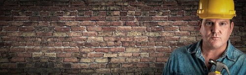 Male contractor in hard hat holding hammer in front of old brick wall banner with copy space