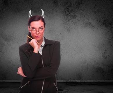 Devil horns drawn on head of red faced young adult woman with pencil in front of grungy wall with copy space