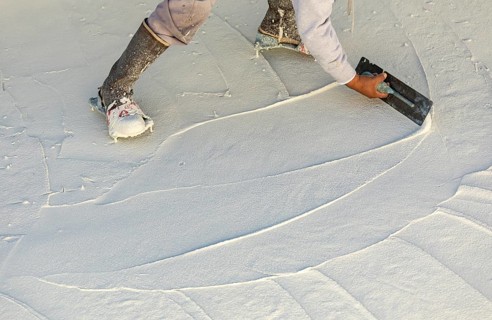 Worker wearing spiked shoes smoothing wet pool plaster with trowel