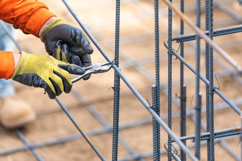 Worker securing steel rebar framing with wire plier cutter tool at construction site