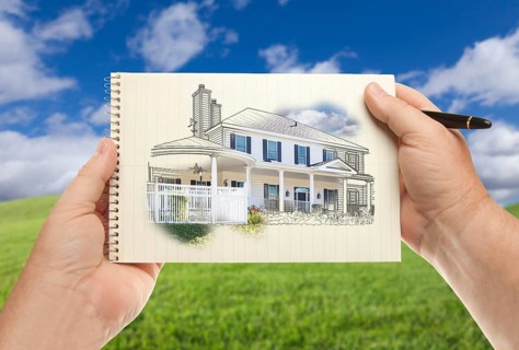 Male hands holding pen and pad of paper with house drawing over empty grass field and sky