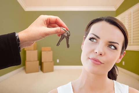 Attractive young woman being handed the keys in empty green room with boxes