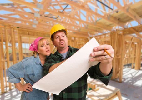 Contractor showing plans to woman on site inside new home construction framing