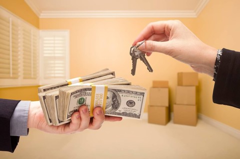 Man and woman handing over cash for house keys inside empty room with boxes