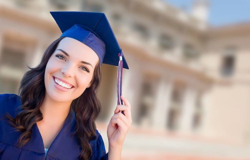 Happy graduating mixed-race woman in cap and gown celebrating on campus