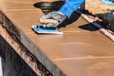 Construction worker using hand groover on wet cement forming coping around new pool