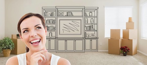 Woman inside room with moving boxes glancing toward entertainment unit drawing on wall