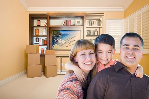 Happy young mixed-race family in room with moving boxes and drawing of entertainment unit on wall