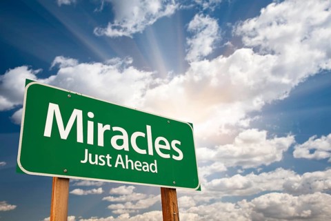 Miracles green road sign against clouds and sunburst