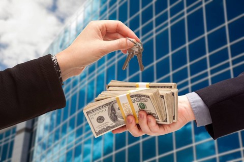 Man handing stack of cash to woman for keys in front of corporate building or apartments