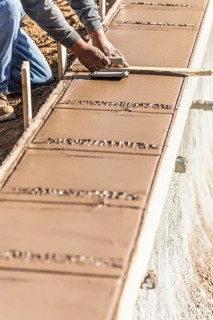 Construction worker using hand groover on wet cement forming coping around new pool