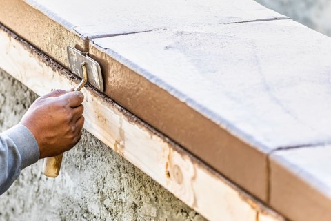 Construction worker using hand groover on wet cement forming coping around new pool