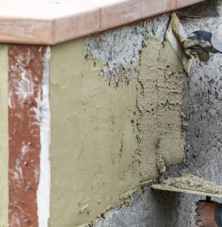 Tile worker applying cement with trowel at pool construction site