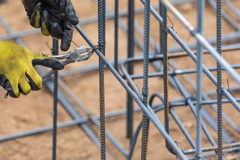Worker securing steel rebar framing with wire plier cutter tool at construction site