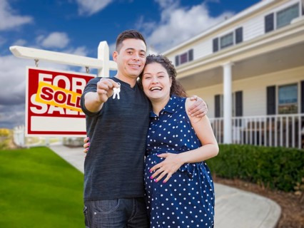 Happy hispanic couple in front of new home and sold real estate sign showing off their house keys
