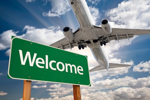 Welcome green road sign and airplane above with dramatic blue sky and clouds