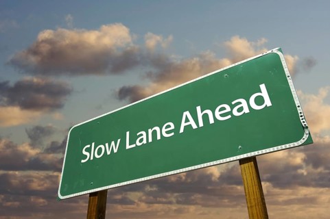 Slow lane ahead green road sign over dramatic clouds and sky