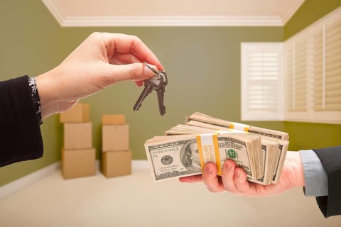 Man and woman handing over cash for house keys inside empty green room with boxes