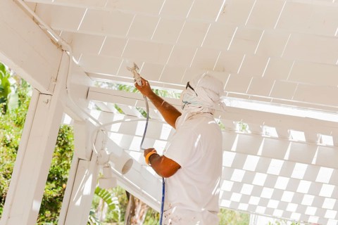 House painter wearing facial protection spray painting A deck of A home