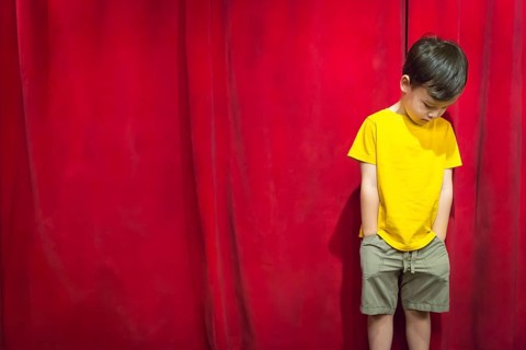 Sad pouting mixed-race boy standing in front of red curtain