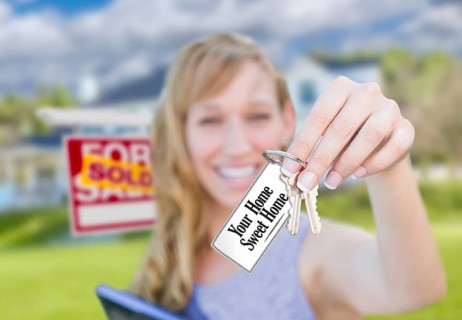 Woman holding new house keys with your home sweet home card in front of sold real estate sign and home